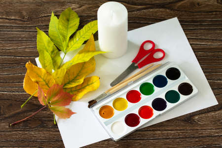 Autumn leaves with a candle and watercolors on wooden background.  Children's art project.の写真素材