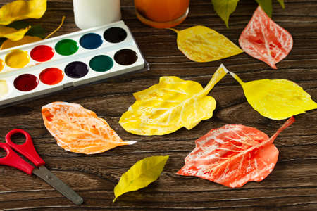 Candle and watercolor paint to create autumn leaves on wooden background. Children's art project.の写真素材