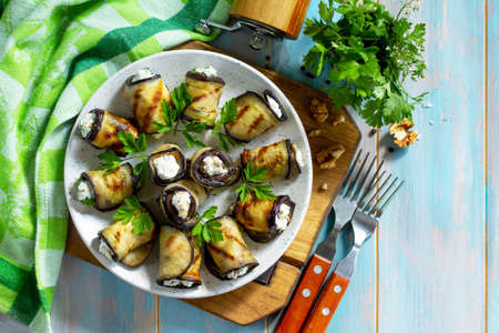 Appetizer stuffed eggplant. Grilled eggplant roll with feta cheese and nuts in a plate on a wooden kitchen table. Top view on a flat background. Copy space.の写真素材