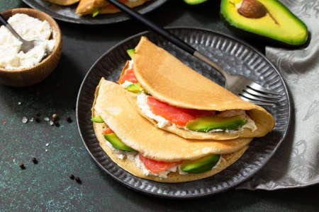 Healthy breakfast or snack. The concept of a healthy and balanced diet. Oat pancakes stuffed with cottage cheese, salmon and avocado in a plate on a stone countertop.の写真素材
