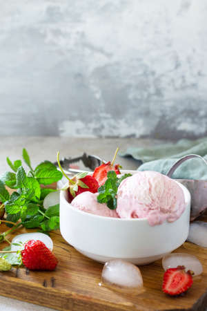 Homemade Organic Strawberry Ice Cream. Strawberry ice cream balls with mint leafon a light stone or...