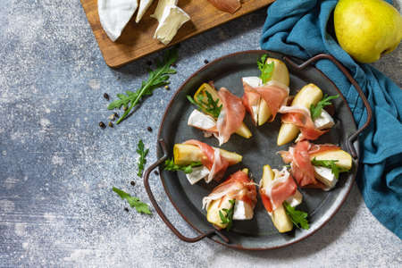Summer snacks. Pear appetizer with jamon, arugula and brie cheese on a light stone table. Top view flat lay background. Copy space.の写真素材