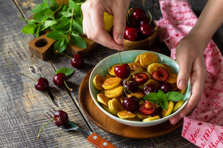 In the hands of a woman breakfast. Mini pancakes with cherries and honey on a rustic wooden table. の写真素材