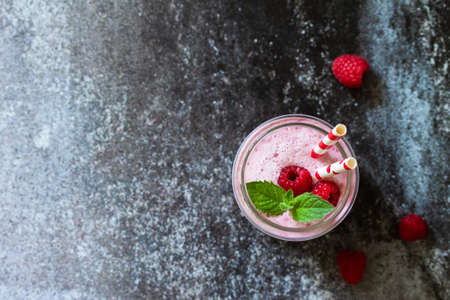 Summer cool milkshake. Raspberry protein shake in glass on a dark background. Top view flat lay...