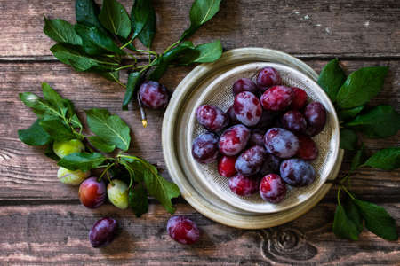 Ripe juicy plums in a bowl on a wooden background. Top view flat lay.の写真素材