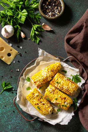 Summer vegan dinner or snacks. Grilled corn with garlic butter, served with cheese on a dark stone table top. Top view flat lay background.の写真素材