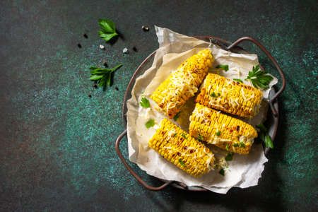 Summer vegan dinner or snacks. Grilled corn with garlic butter, served with cheese on a dark stone table top. Top view flat lay background. Copy space.の写真素材