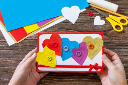 Child holding Greeting card with a hearts Valentine's Day, day mother or birthday present on wooden table. Childrens art project crafts for children. Craft for kids.の写真素材