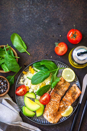 Grilled salmon fillet close-up with couscous, salad fresh vegetables and avocado on dark background. Top view flat lay. Copy space.の写真素材