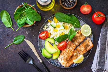 Grilled salmon fillet close-up with couscous, salad fresh vegetables and avocado on dark background. Top view flat lay.の素材 [FY310163556126]