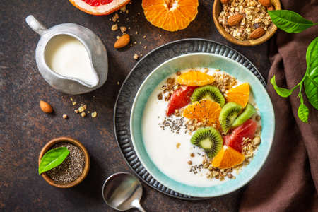 Healthy breakfast. Bowl of homemade granola with yoghurt, fresh fruit, nuts and chia seeds on a dark stone tabletop. Copy space. Top view flat lay.の写真素材