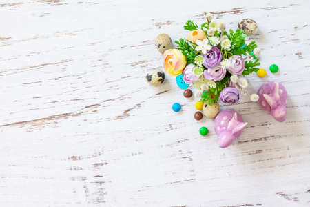 Happy Easter background. Spring flowers, easter eggs, sweets and easter bunny on a white wooden...