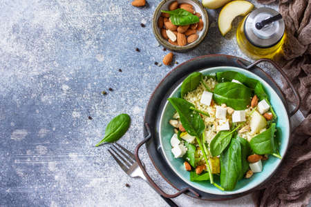 Couscous salad with pear, spinach, almonds, feta cheese and vinaigrette sauce on a gray stone table. Top view flat lay. Copy space.の写真素材