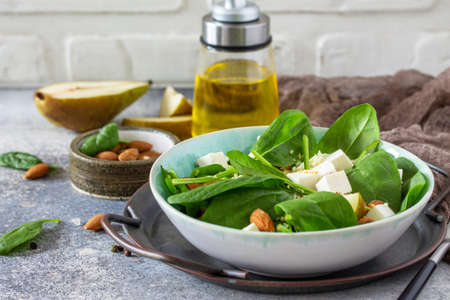 Couscous salad with pear, spinach, almonds, feta cheese and vinaigrette sauce on a gray stone table.の写真素材