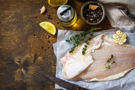 Seafood, raw white fish fillet for cooking. Fresh fillet Pangasius with spices, lemon and thyme on rustic wooden table. Top view, flat lay. Copy space.の写真素材