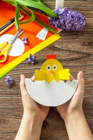 Child is holding an paper Easter egg gift with a chicken. Easter handmade Project of children's creativity, handicrafts, crafts for kids.の写真素材
