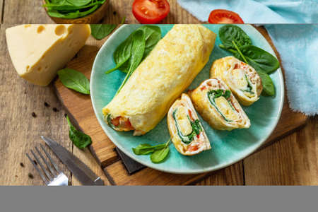 Japanese cuisine. National Japanese dish Omelet tamago yaki for breakfast. Rolled egg with spinach, tomato and cheese on a wooden table.の写真素材