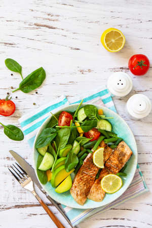 Grilled salmon fillet with spinach, cucumber, tomato and avocado salad on a white wooden table. Top view, flat lay. Copy space.の写真素材