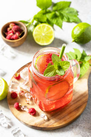 Soft drinks, healthy beverage. Refreshing summer glasses drink raspberry with mint lime and ice on a...