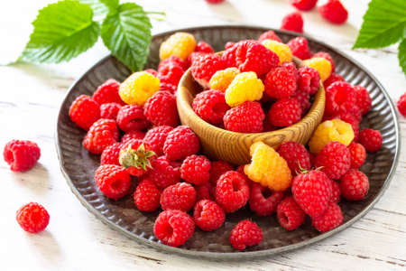 Ripe juicy sweet berries of yellow and red raspberries on a white rustic table.