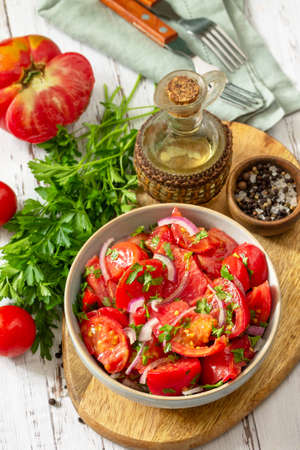Summer snack or lunch. Fresh tomato salad with onions, herbs and olive oil on a white wooden table.の写真素材