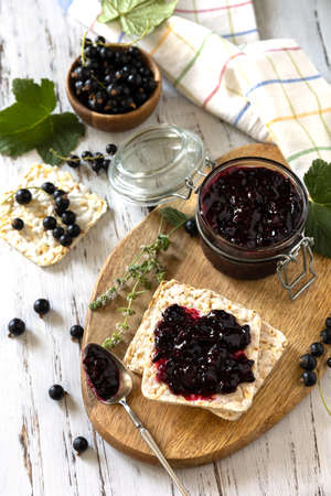 Blackcurrant jam in a glass jar and gluten-free crispbread on a rustic table.の写真素材