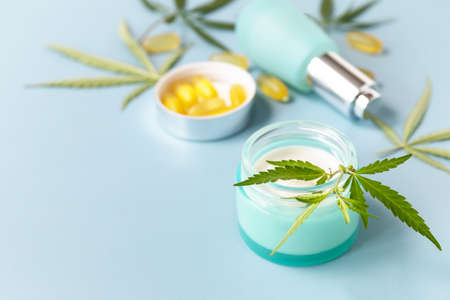 Herbal Alternative Medicine Concept, cosmetics CBD oil. Cannabis leaf skincare cosmetic product. Moisturizing cream, Serum, capsules oil on a pastel blue background. Copy space.の写真素材