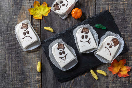 Homemade baked halloween party. Funny cookies in white chocolate glaze ghost on a wooden table. Top view flat lay background. Copy space.の写真素材