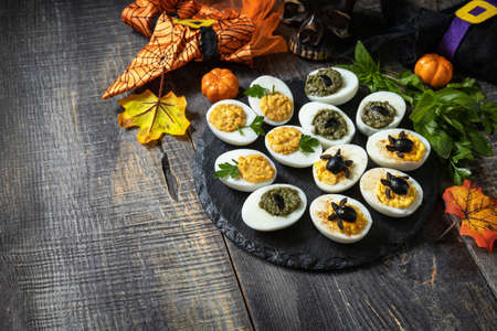 Halloween funny idea for party food. Halloween creative set stuffed eggs on a wooden table. Copy...