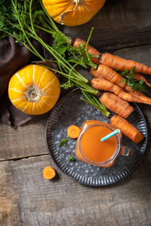 Fresh natural mixed juice, healthy food concept. Glass jar of fresh carrot juice with fresh carrots and pumpkin on a wooden rustic table. Top view flat lay background.の写真素材