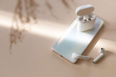Wireless technology, modern tech. Minimal shot smartphone and of a pair of white wireless headphones, dried grass on a pastel neutral colors background. Copy space.の写真素材
