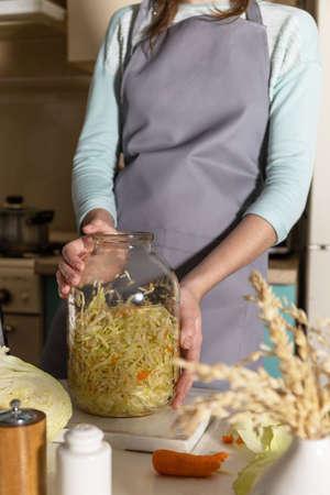 Sauerkraut canning. A young woman prepares homemade sauerkraut with carrots in the kitchen. Fermented food.の写真素材
