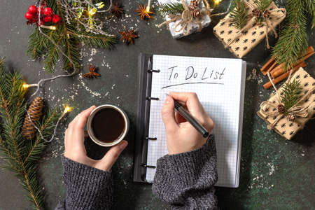 The woman writes in notebook with empty to do list and cup of coffee on xmas dark stone tabletop. New year goals background. Flat lay.の写真素材