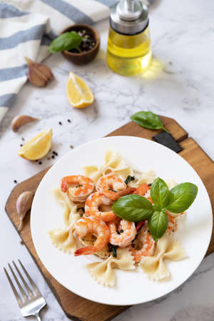 Mediterranean cuisine, seafood diet. Italian farfalle pasta with prawns garlic, basil and lemon on a marble tabletop.の写真素材