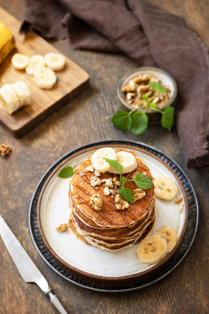 Celebrating pancake day, american breakfast. Delicious homemade banana pancakes with nuts and caramel on rustic wooden table.の写真素材