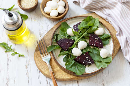 Healthy diet salad with arugula, spinach, beetroot, mozzarella and vinaigrette dressing on a wooden table. Low calories keto dieting meal.の写真素材