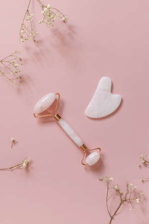 Rose quartz facial massage roller over pink background with gypsophila flowers. Massage tools with jade stone, anti-aging, anti-wrinkle beauty skincare tool. Top view flat lay.の写真素材