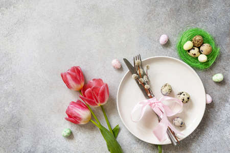 Festive Easter table setting with painted eggs, spring flowers and cutlery on light gray tabletop....