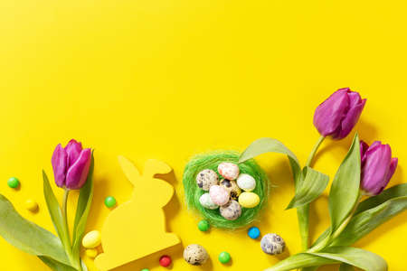 Colorful Easter background. Holiday greeting card with painted eggs, purple tulip. Top view flat...