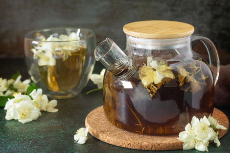 Therapeutic herbal tea. Hot green tea with jasmine flowers in a glass teapot on a stone table.