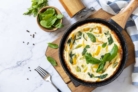 Spinach and cheese omelette. Frittata made of eggs, paprika and spinach in a frying pan on a marble countertop. view from above. copyspace.の写真素材