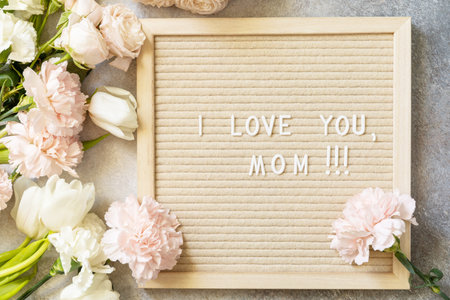 Happy Mother's Day. Letter I LOVE MOM on letterboard and beautiful spring flowers on light...