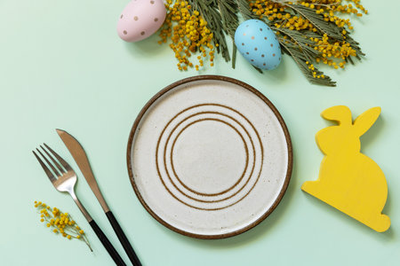 Easter table setting. Plate with easter eggs and mimosa on a pastel green background. Happy Easter...