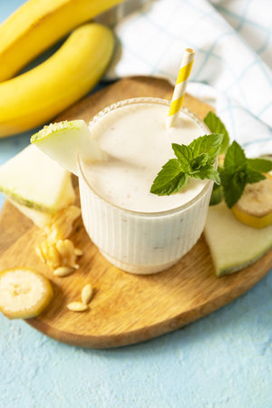 Banana smoothie with melon in drinking glass on wooden board on a stone background. Detox menu. Fresh seasonal smoothies. copyspace.の写真素材