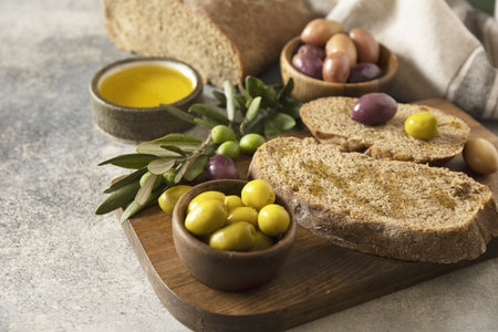 Mediterranean snack with mixed olives, olive oil, and rustic bread on wooden board.の写真素材