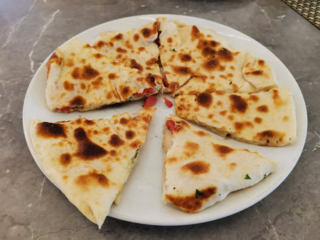 Sliced toasted stuffed flatbread on white plate photographed from angled top for menu background and...