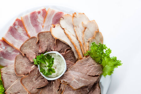 Sliced bacon and ham with lettuce on white plateの写真素材