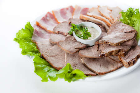 Sliced bacon and ham with lettuce on white plateの写真素材