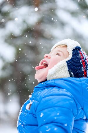 Outdoor portrait Happy child catches snowflakes mouth in winter parkの写真素材