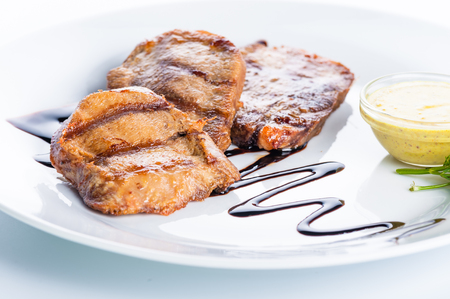 Grilled beef steak with sauce and greens on a white backgroundの写真素材